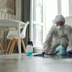 Specialized cleaning person in protective suit disinfecting a floor indoors for hygiene and safety.