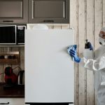 A person in protective gear cleaning a kitchen appliance to ensure hygiene.